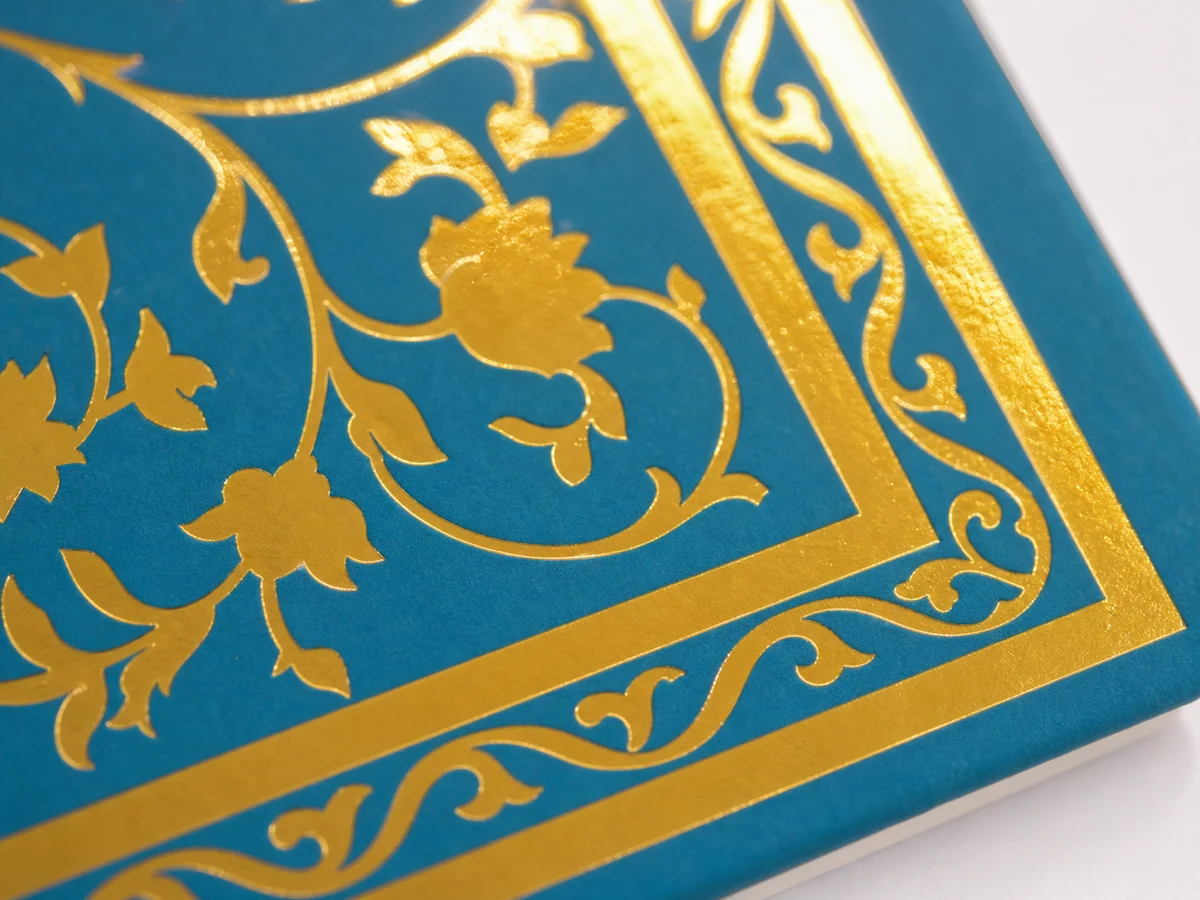 Macro close-up of a gold foil border on a teal notebook cover
